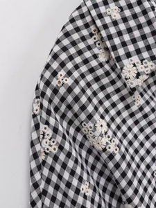 Détail macro d'une broderie florale blanche sur une chemise à carreaux vichy noir