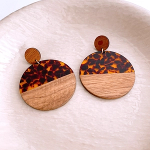 Detail of round tortoiseshell and wood pendant earrings on a white ceramic plate