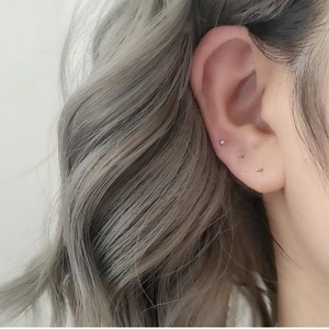 Close-up of minimalist tiny gold and silver stud earrings on a model's ear