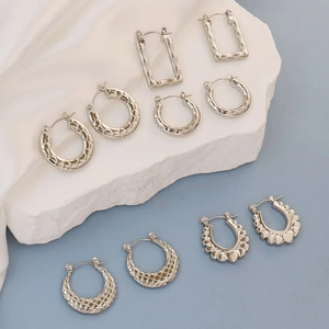 Detail view of five assorted silver geometric hoop earrings on a tiered stone stand