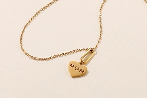 Detail of gold heart pendant with MOM engraving on textured beige background