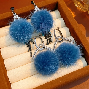 Detail of blue fur ball earrings with diamond rhombus accents in jewelry box