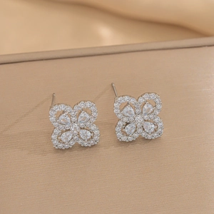 Detailed close-up of clover stud earrings with sparkling cubic zirconia on a textured surface