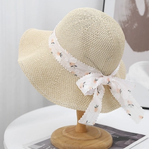 Dettaglio cappello da sole in maglia beige con nastro floreale e tesa larga a onde