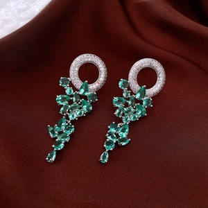 Macro detail of silver drop earrings with green pear-shaped stones and white zircons
