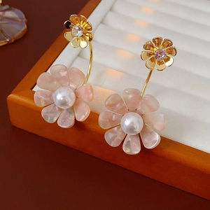 Detail view of gold flower earrings with pink petals and pearl center on white velvet