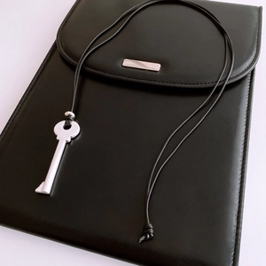 Detail of minimalist black faux leather pouch with silver metal key pendant necklace