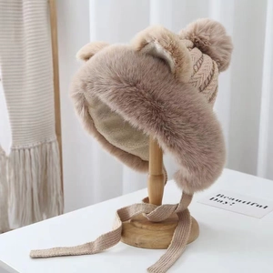 Detail of khaki plush winter hat with cute bear ears and fuzzy pompom on a wooden stand