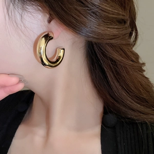 Close-up of elegant gold C-shaped chunky hoop earrings worn for a minimalist stylish look