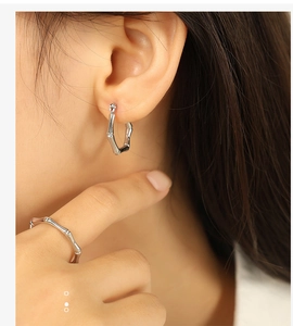 Close-up of silver bamboo-style earrings and ring on a model with natural lighting
