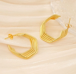Detailed view of layered geometric gold earrings on white silk with textured glass