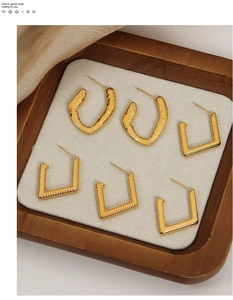 Close-up of geometric textured gold-plated titanium steel earrings in a wooden tray