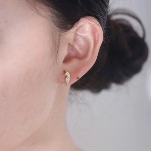 Close-up of a gold seahorse earring with zircon inlay worn on a model's earlobe