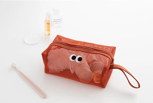 Orange mesh toiletry bag with googly eyes holding toothbrushes on a white desk
