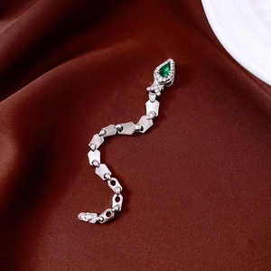 Macro shot of silver snake pendant with green pear-cut zircon on red silk background
