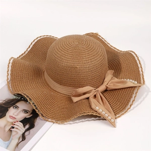 Detail of a brown woven straw hat with pearl bow tie and white lace wave edge