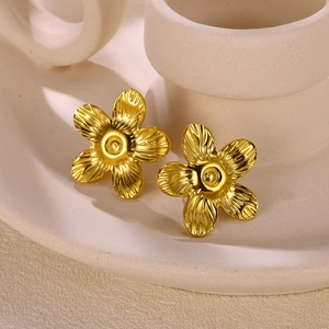 Macro detail of gold-plated sunflower stud earrings on a beige ceramic surface