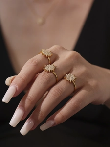 Detail of a gold star-shaped ring with 5A zircon inlay worn by a model on black background