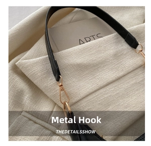 Close-up of black leather bag strap with pale gold metal hook and textured leather detail