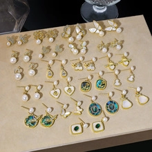 Detailed close-up of various vintage gold earrings with pearls and rhinestones on a beige board