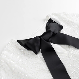 Détail d'une robe blanche à paillettes avec un grand nœud décoratif en ruban noir à l'encolure
