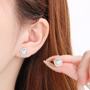 Détail d'une boucle d'oreille perle blanche ronde avec bordure en métal argenté