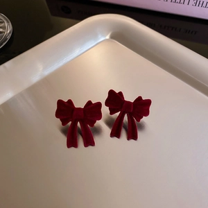 Close-up of deep red velvet bow earrings placed on a premium silver metal tray