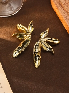 Macro detail of golden leaf-shaped earrings with artistic hammered texture and finish