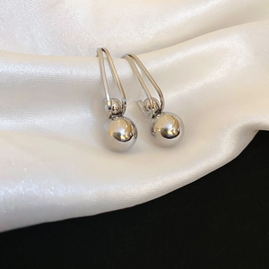 Macro detail of minimalist polished silver ball drop earrings on white silk