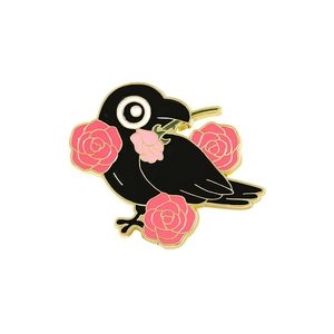 Enamel black crow pin with pink roses and gold metal edging on a white background