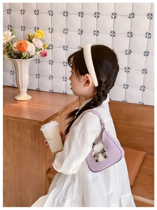 Detail of purple PU shoulder bag with silver bow decoration and smooth leather texture