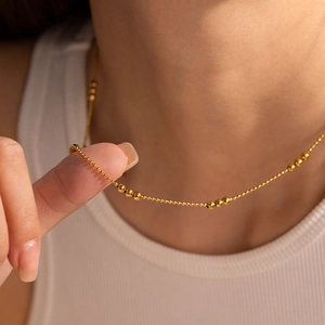 Close-up of a delicate 18K gold-plated ball chain necklace worn on the collarbone