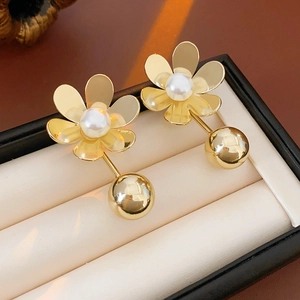 Gros plan de boucles d'oreilles fleurs dorées avec perles et boules sur un coussin