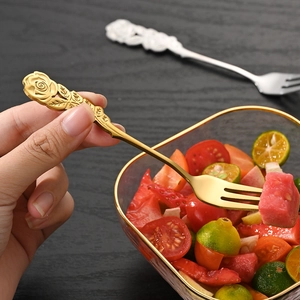 Golden stainless steel dessert fork with rose engraving held over a fruit salad bowl
