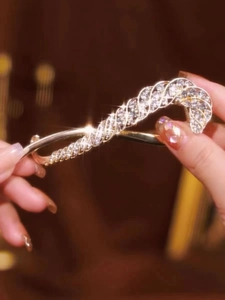 Detailansicht einer goldenen Haarklammer mit glitzernden Strasssteinen in den Händen
