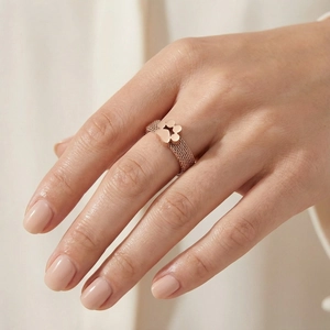 Detail of rose gold mesh ring featuring a clover charm on the hand of a female model