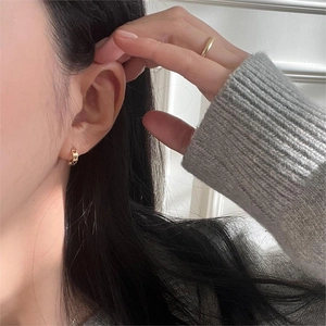 Detail of gold heart cutout hoop earrings and slim ring styled with a grey sweater