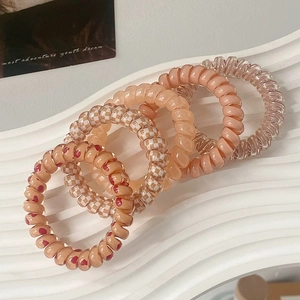 Macro detail of elastic spiral hair ties in peach and checkerboard patterns on a stand