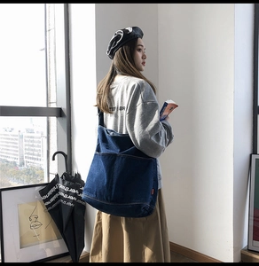 Deep blue denim oversized shoulder bag with orange label detail on a model