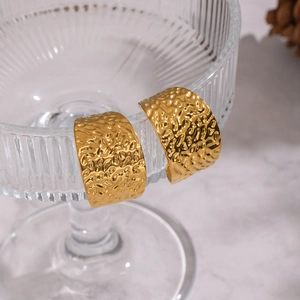 Boucles d'oreilles créoles dorées avec texture martelée sur un verre strié