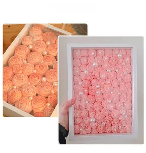Detail view of handmade pink paper roses with pearl accents in a white wooden display frame