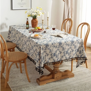 Detail shot of the blue floral print linen tablecloth with black tassel fringe on wood