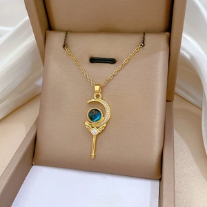 Detailed close-up of a gold crescent moon magic wand pendant with blue gem and diamonds