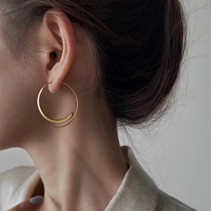 Detail of matte gold spiral hoop earrings on model showing artistic metal texture