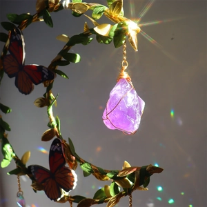 Detail of handcrafted amethyst raw stone pendant with gold wire wrap and butterfly accent