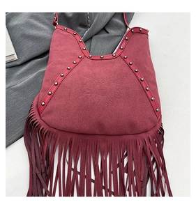 Detail of bohemian dark red suede bag with sun face embossing, metal studs and tassels