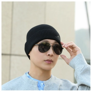 Close-up of a stylish black knitted beanie worn by a man with sunglasses outdoors.