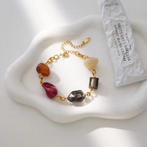 Detail of a vintage resin bracelet with colorful stones and gold chain on a ceramic tray