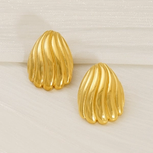 Détail macro de boucles d'oreilles dorées 18K avec motif vagues sur fond de tissu doux