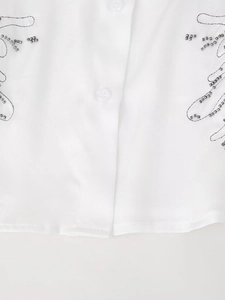 Close-up of white woven shirt showing round buttons and detailed silver bead embroidery